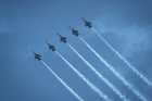 Five U.S. Navy Blue Angel planes flying in a straight line through the sky with white smoke coming out the rear of the planes